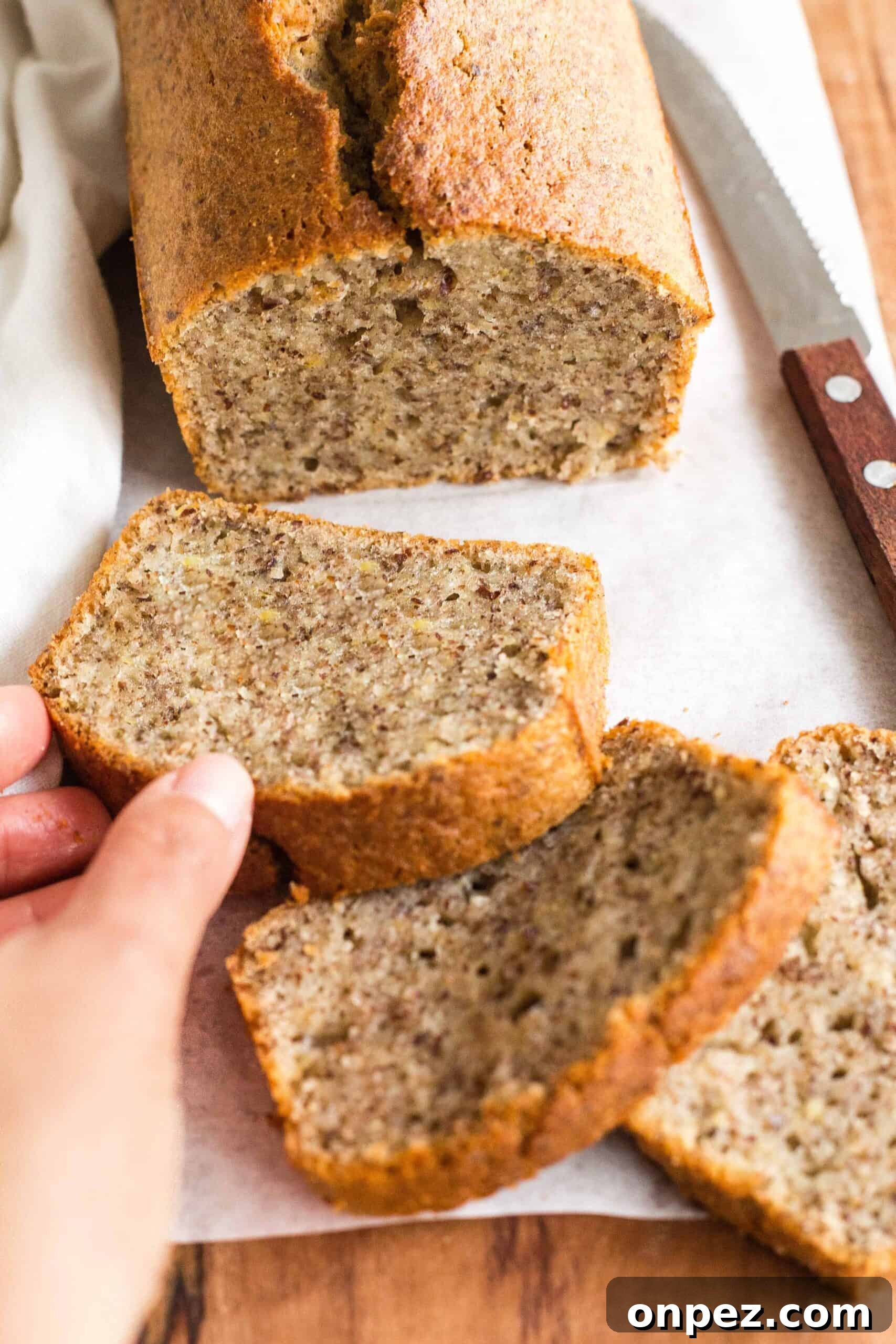 Easy Flaxseed Bread (Gluten-Free, Dairy-Free) Reaching for a slice of flax bread from a wooden board.