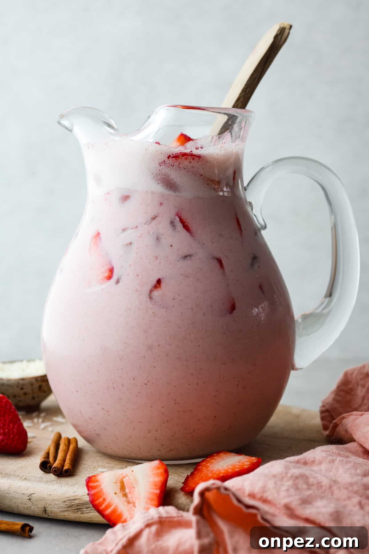 Creamy strawberry horchata in a glass pitcher. Close view of strawberry horchata in a glass pitcher with a large gold spoon for stirring.