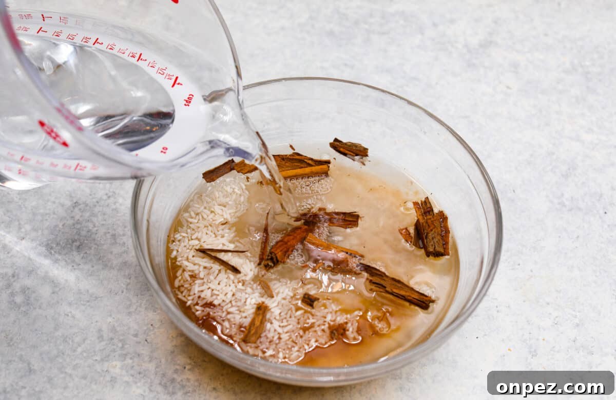 Combine rice, cinnamon sticks, vanilla, and hot water for strawberry horchata. Process photo of water pouring into a bowl of rice and cinnamon sticks.