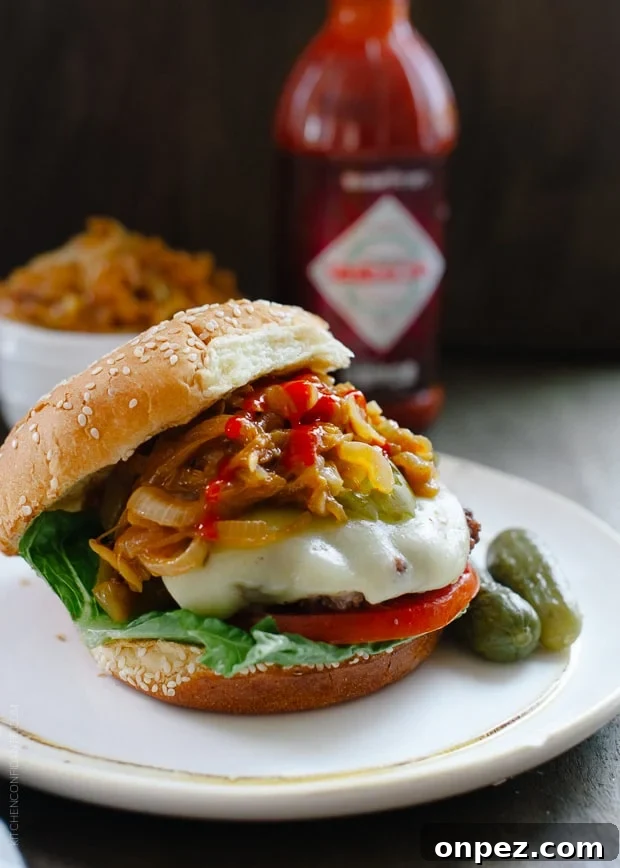 Sriracha Caramelized Onions topping a large burger on a white plate.