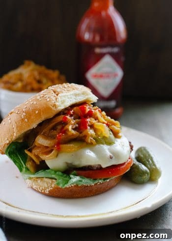A hamburger loaded with toppings like cheese, tomato, pickles, and Sriracha Caramelized Onions.