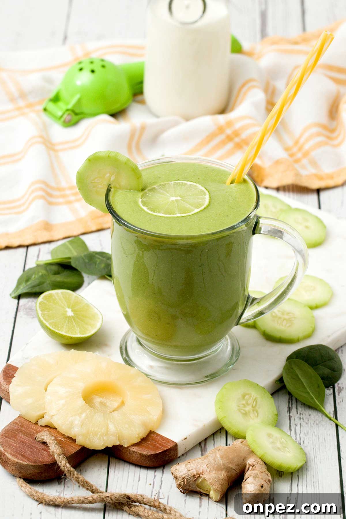 A detox smoothie with cucumber pineapple ginger and lime with a yellow straw in a glass.