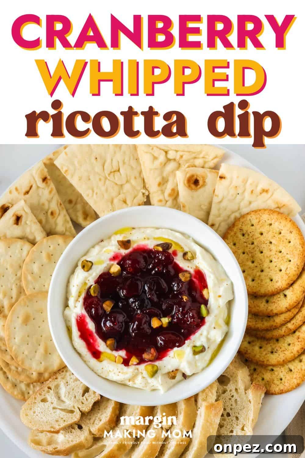 overhead view of a bowl of cranberry whipped ricotta dip on an appetizer platter, surrounded by crackers, bread slices, and pita triangles.