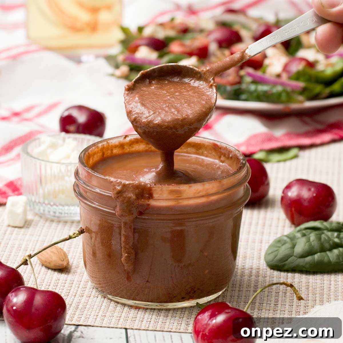 A spoon full of cherry balsamic vinaigrette with fresh cherries.