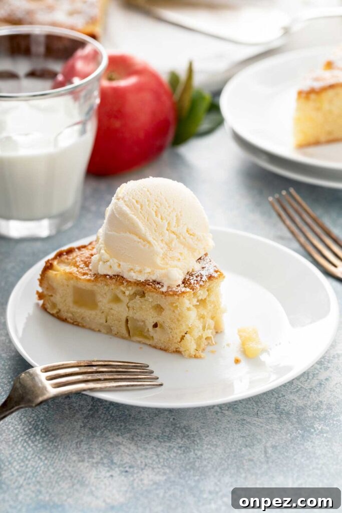 Slice of cake with apples topped with vanilla ice cream on a white plate