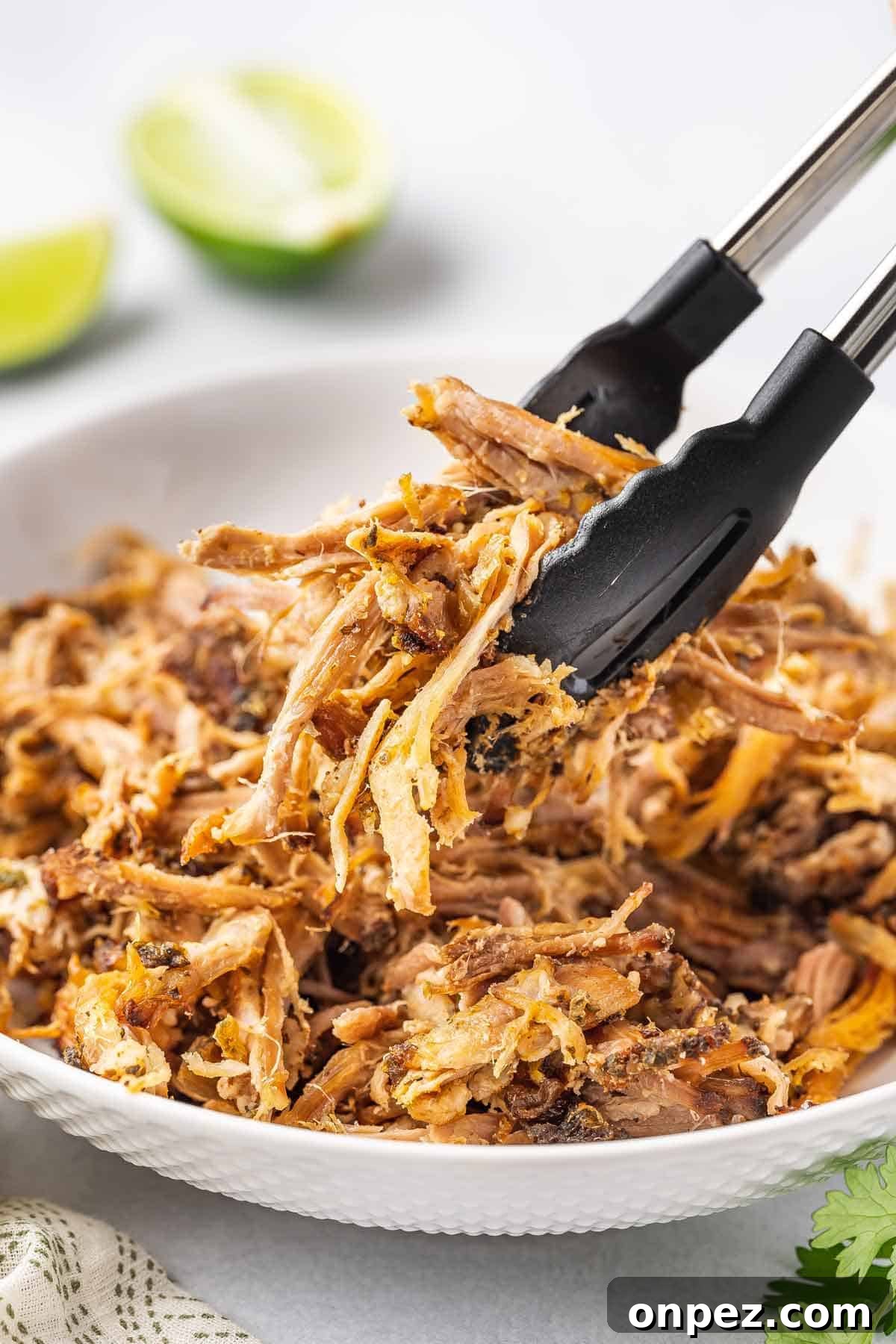 A pair of tongs lifting up some shredded slow cooker carnitas.