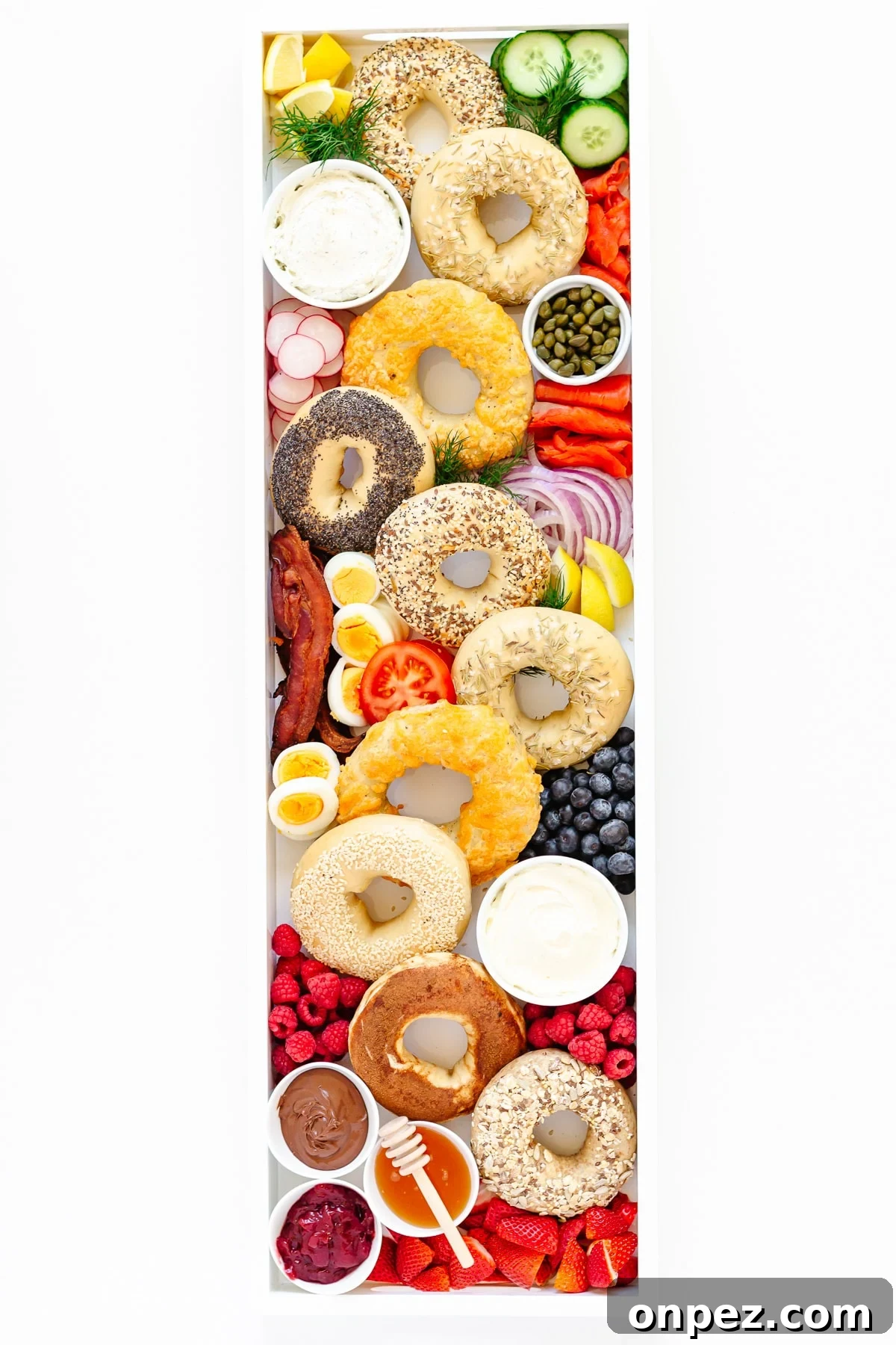 Variety of different bagels and sweet and savoury toppings arranged on a long white tray.