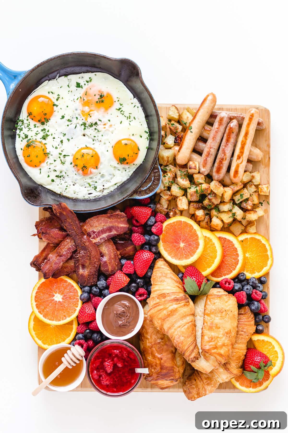 Bacon and eggs breakfast grazing board featuring fried eggs, bacon, breakfast sausages, croissants, hash browns, fresh fruit and spreads.