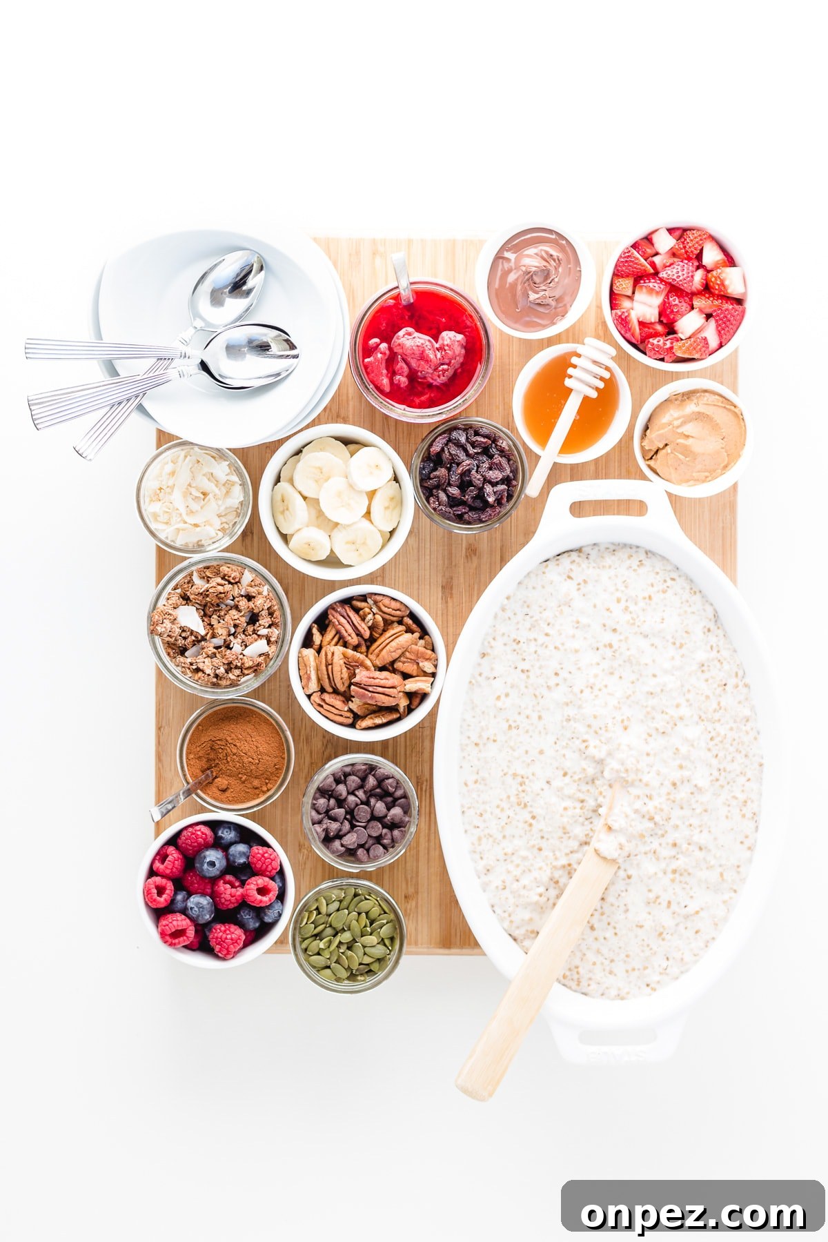 Wooden board topped with a large dish of steel cut oats, variety of small bowls of different toppings and a stack of serving bowls and spoons.