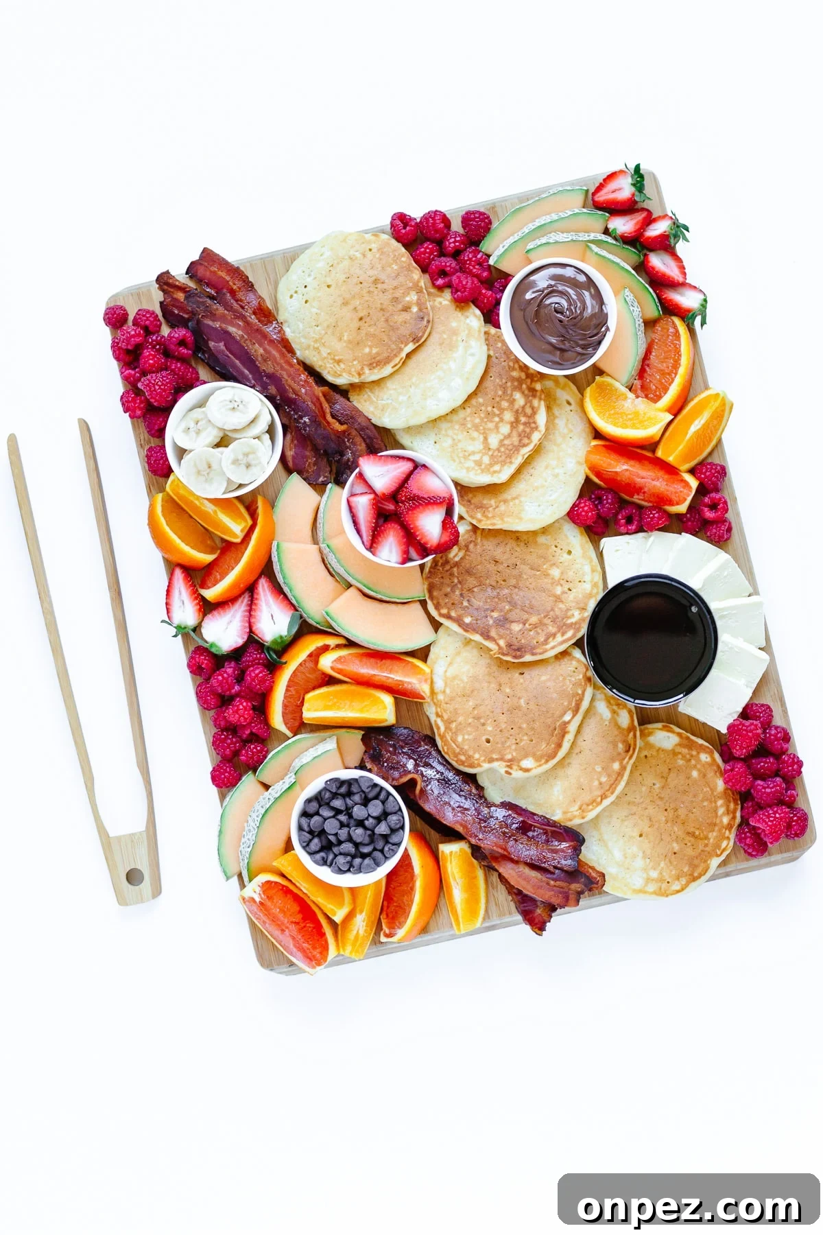 Pancake charcuterie board and wooden tongs on a white background.