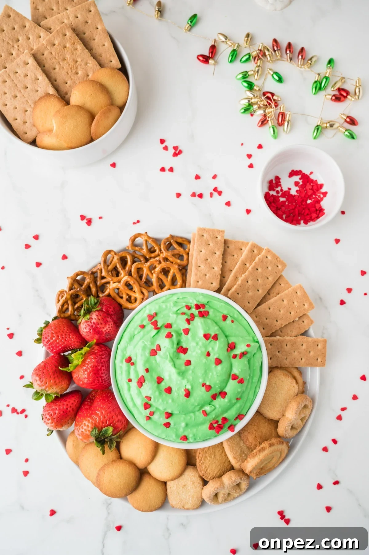 Creamy Grinch Dip Recipe for Holiday Parties 2 An overhead image of grinch dip in the center with an assortment of crackers, biscuits, pretzels, and strawberries on the side.