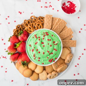 Creamy Grinch Dip Recipe for Holiday Parties 10 An overhead image of grinch dip in the center with an assortment of crackers, biscuits, pretzels, and strawberries on the side.