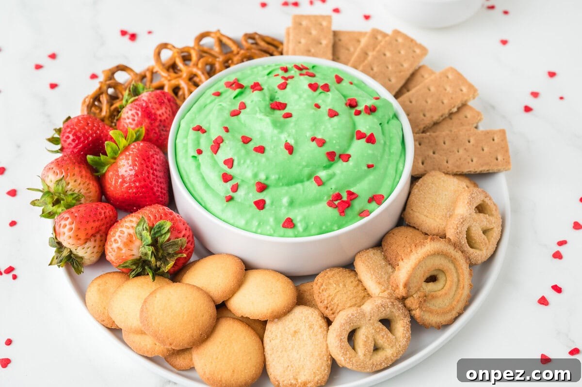Creamy Grinch Dip Recipe for Holiday Parties 9 A close up image of grinch dip in the center with an assortment of crackers, biscuits, pretzels, and strawberries on the side.