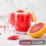 Glass of blood orange whisky sour, garnished with a slice of blood orange, with an orange slice ice cubes and rose petals in the foreground.