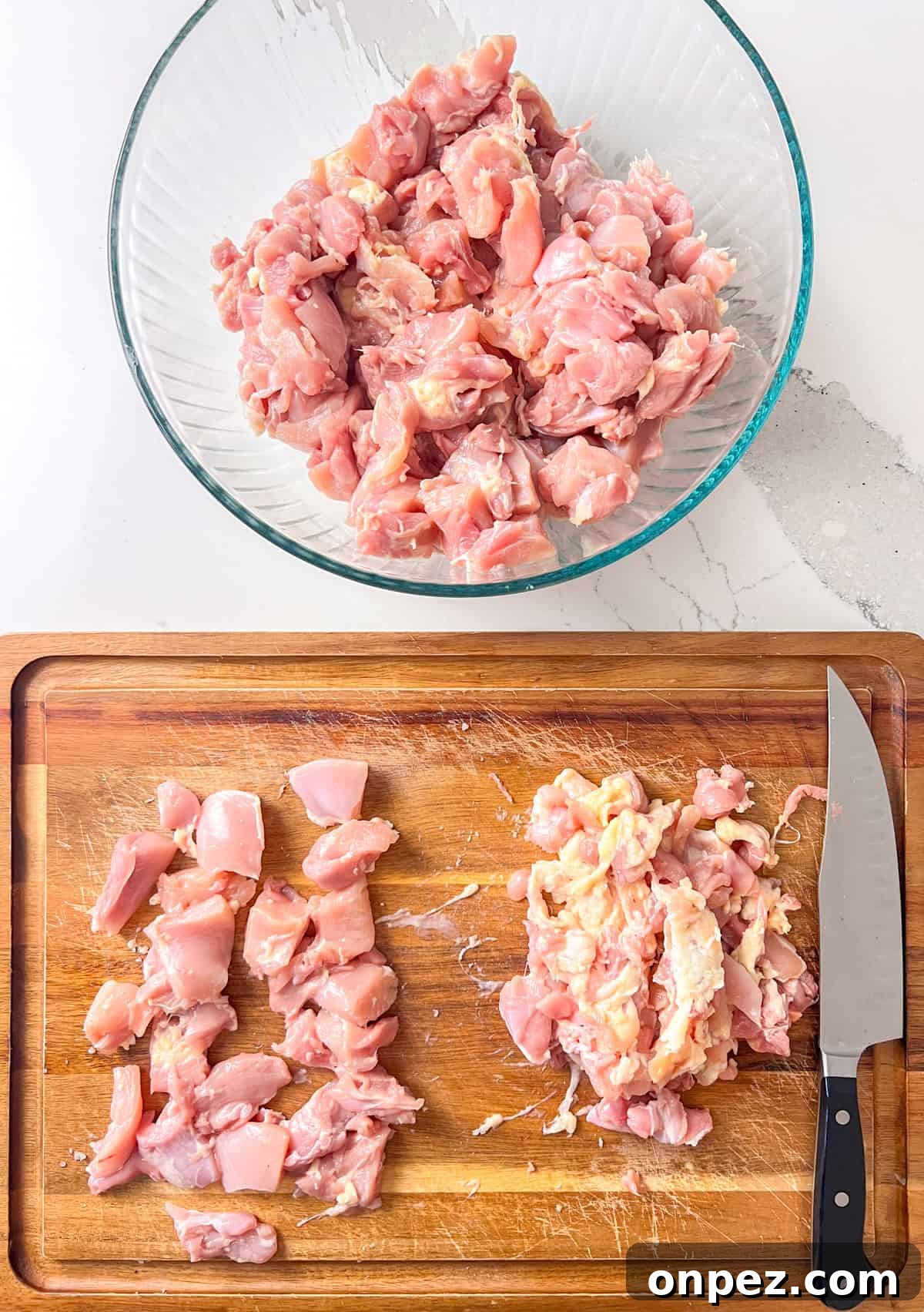 Raw chicken thighs being cut up with cubes.