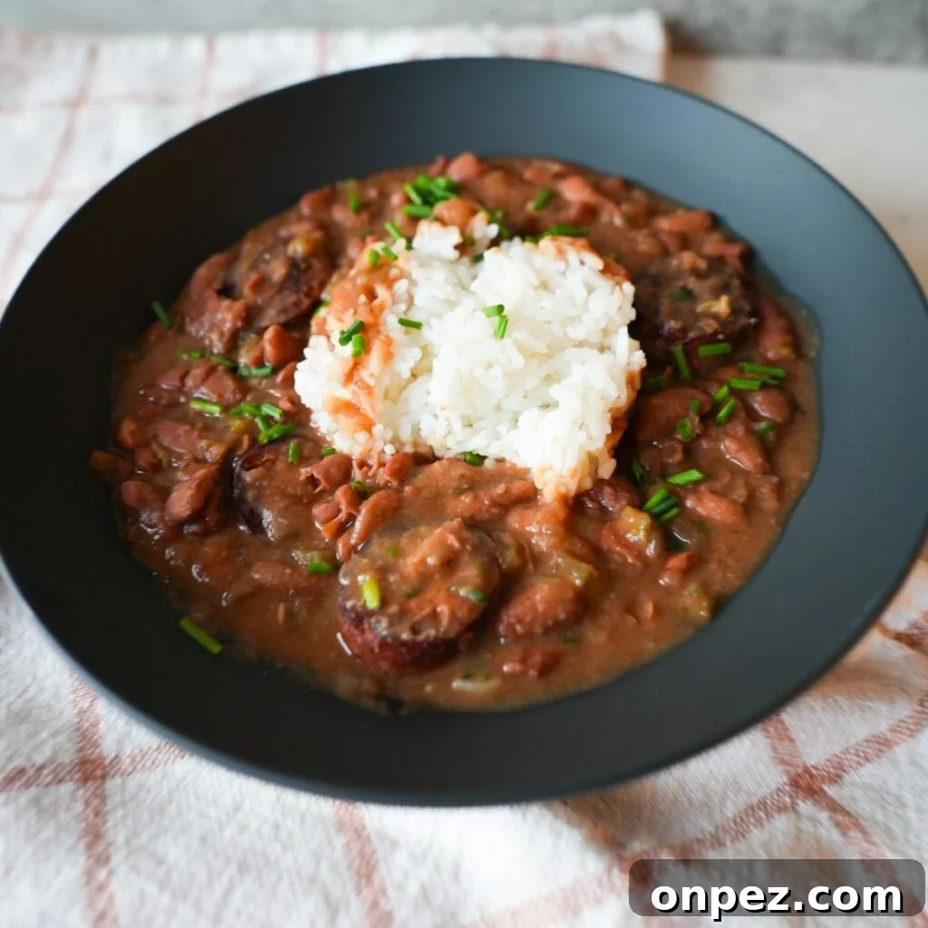 Authentic New Orleans Red Beans and Rice 2 Bowl of red beans and rice with sliced sausage, garnished with chopped chives and parsley on top of fluffy white rice.