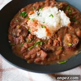 Bowl of red beans and rice with sliced sausage, garnished with chopped chives and parsley on top of fluffy white rice.
