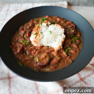 Authentic New Orleans Red Beans and Rice 7 Bowl of red beans and rice with sliced sausage, garnished with chopped chives and parsley on top of fluffy white rice.