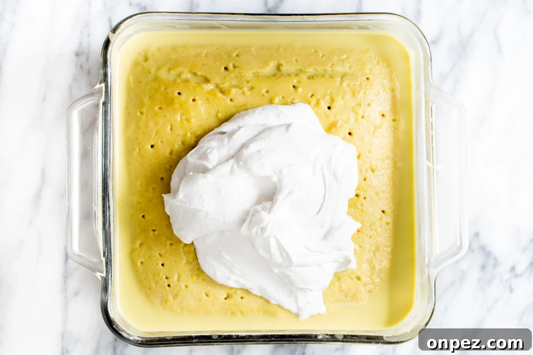coconut whip being spread over vegan tres leches in a pyrex pan