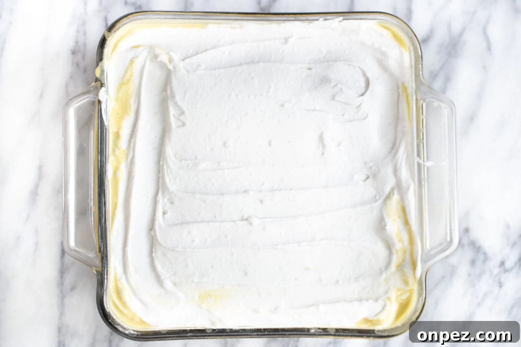 vegan coconut whip being spread over a soaked sponge cake to make tres leches