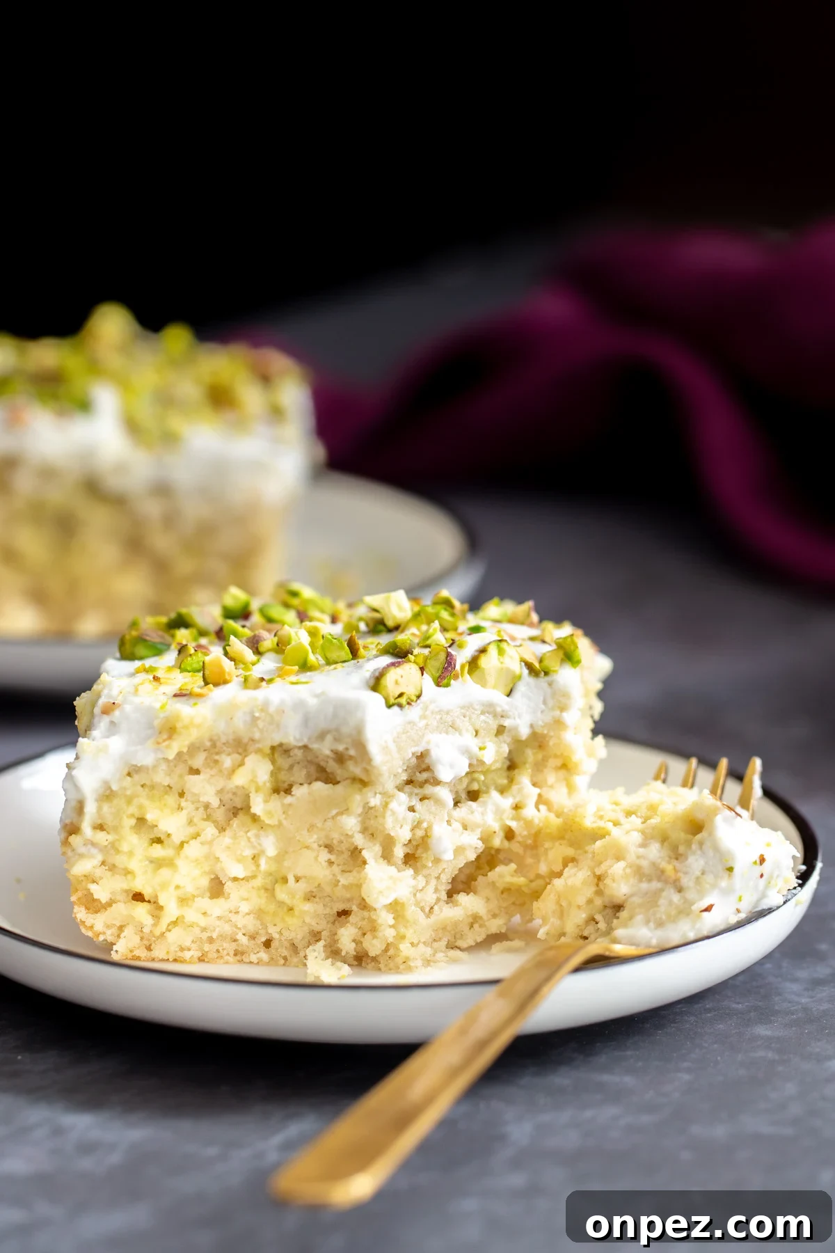a half eaten piece of vegan ras malai tres leches cake with a golden fork on the side