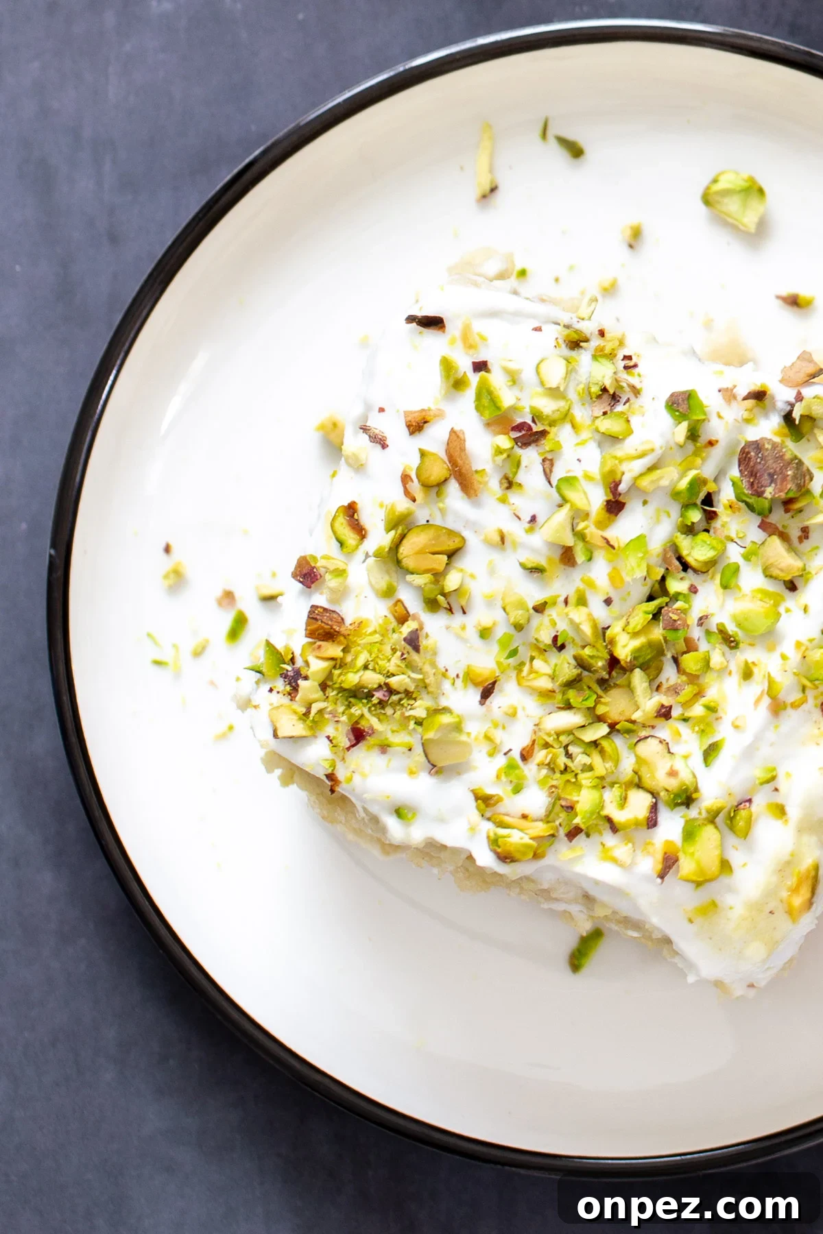 a slice of vegan ras malai tres leches sprinkled with pistachios served on a white plate
