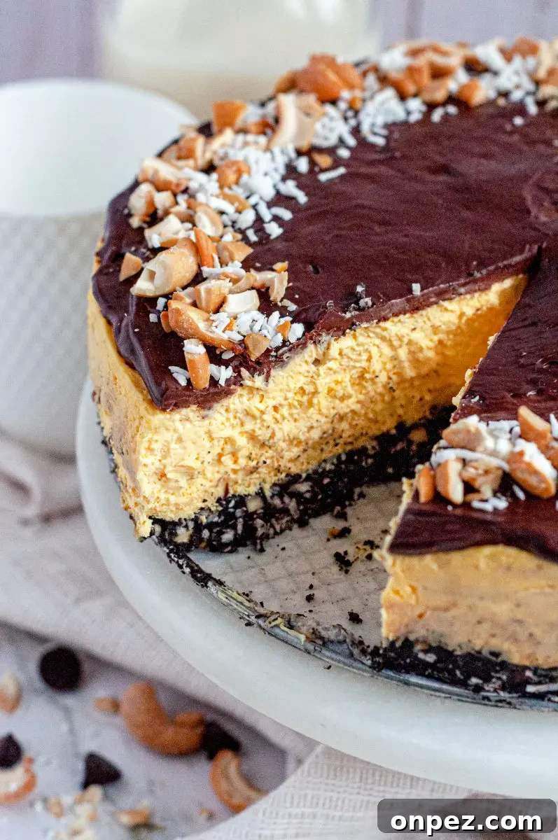 No-Bake Vegan Gluten-Free Nanaimo Bar Cheesecake 4 A no-bake nanaimo bar cheesecake. it has three layers. The bottom layer is a chocolate crust, the middle layer is a yellow custard cheesecake, and the top is a thin layer of dark chocolate topped with white shredded coconut and yellow salted cashews. There is a slice cut out of the cheesecake.