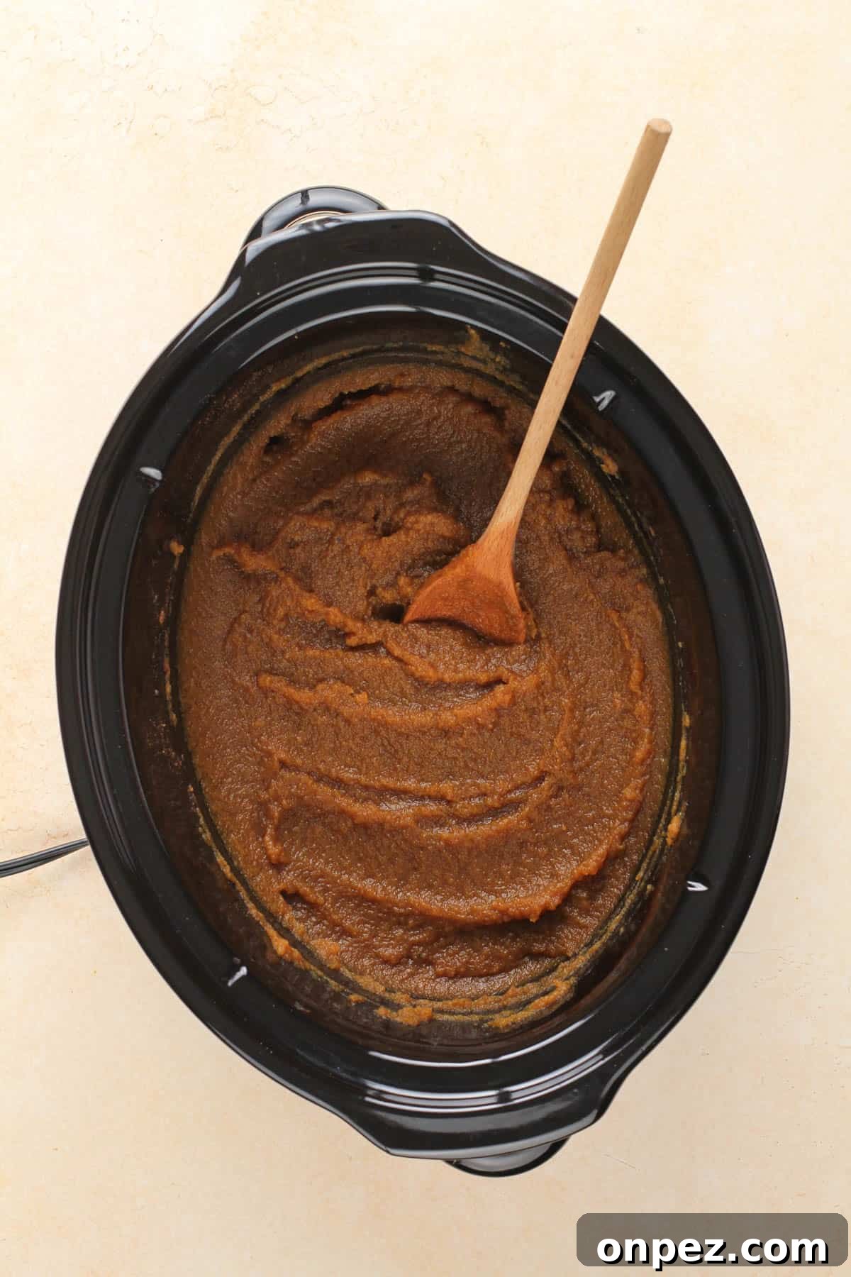 a slow cooker containing cooked pumpkin butter and a wooden spoon