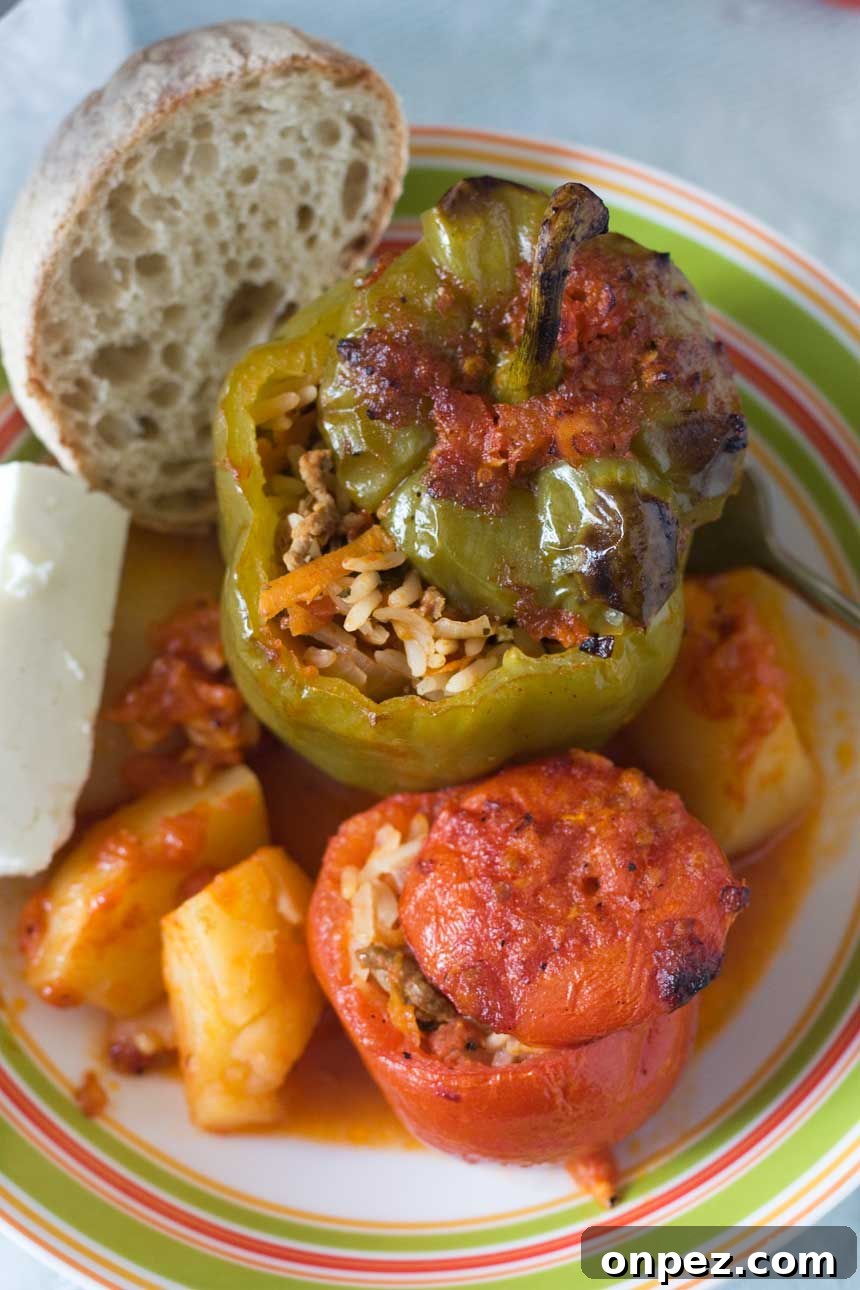 An overhead shot of Greek stuffed tomatoes and peppers in a colourful dish with bread and feta cheese