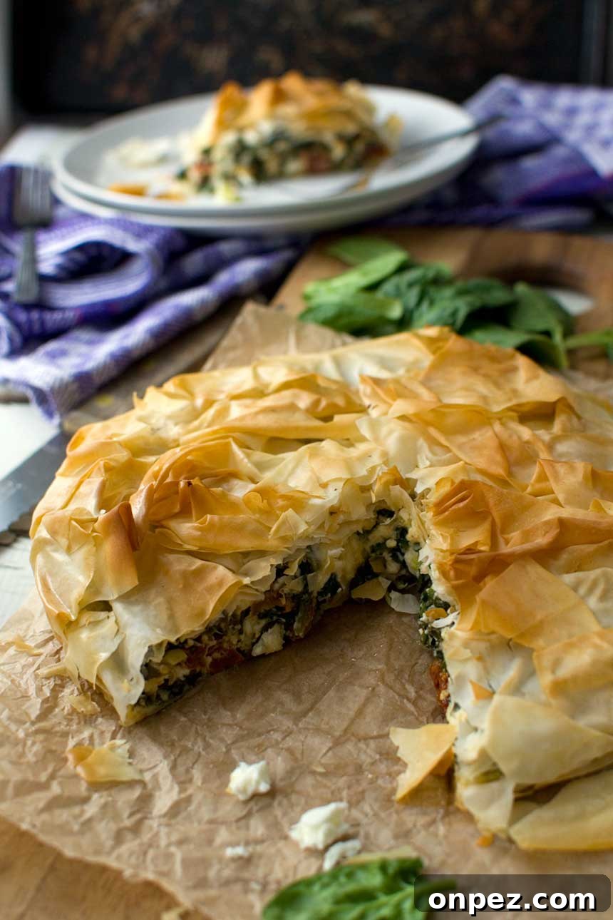 Closeup of a spinach and feta filo pie on baking paper with a piece cut out.