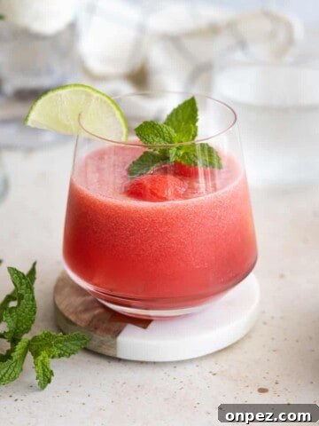 A watermelon mint cocktail in a rocks glass garnished with mint and a lime slice.