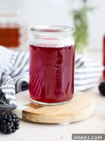 Blackberry simple syrup in a small glass jar with a blue and white striped linen.