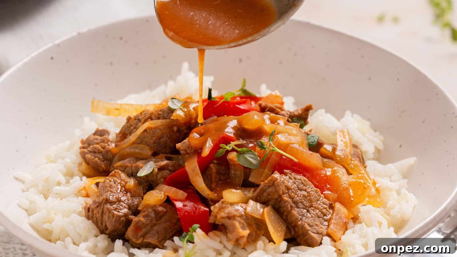 Pouring savory sauce over a bowl of rice topped with beef and bell peppers.