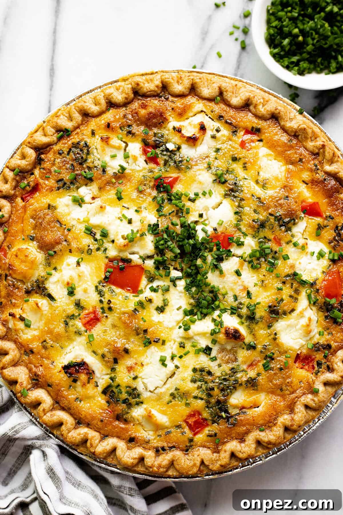 Quick Breakfast Quiche Recipe 2 Overhead shot of a quiche with red peppers and potatoes garnished with sliced chives.