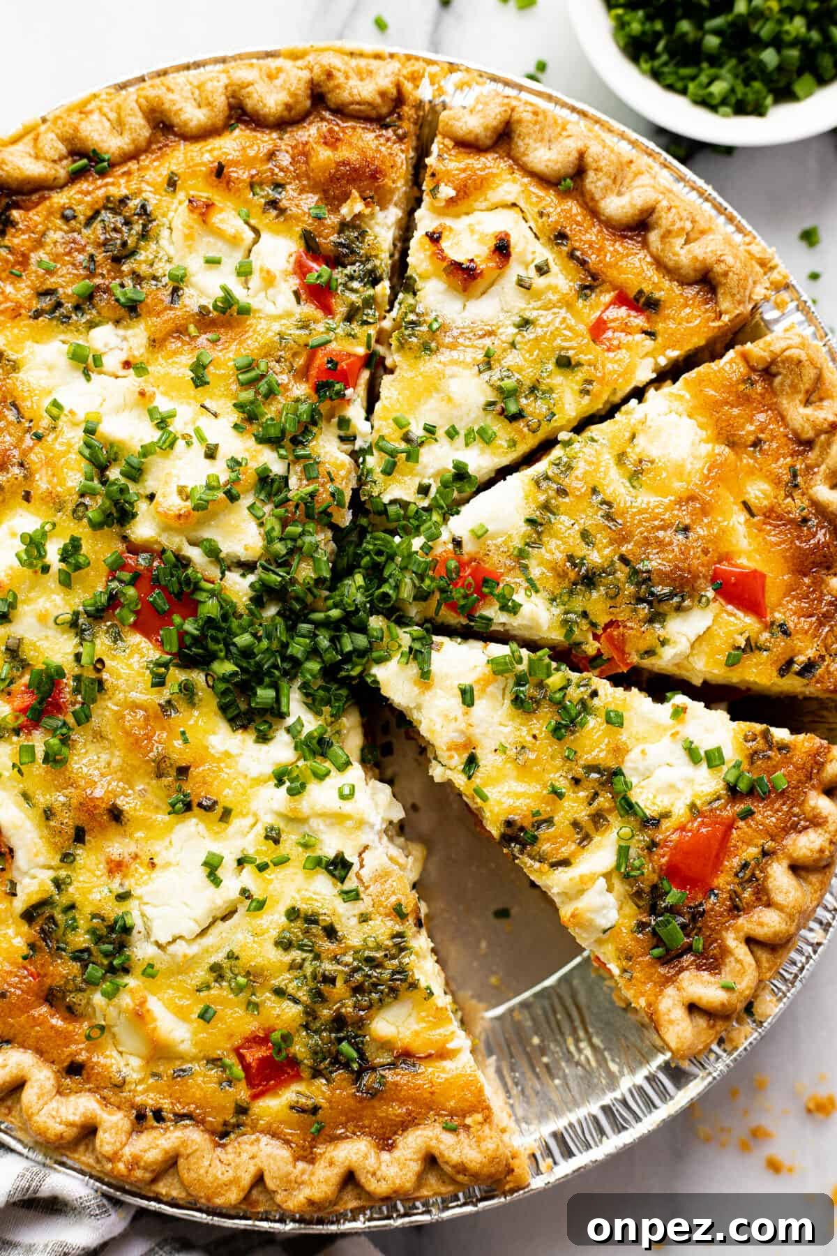 Quick Breakfast Quiche Recipe 11 Overhead shot of a sliced quiche with red peppers and potatoes garnished with sliced chives.