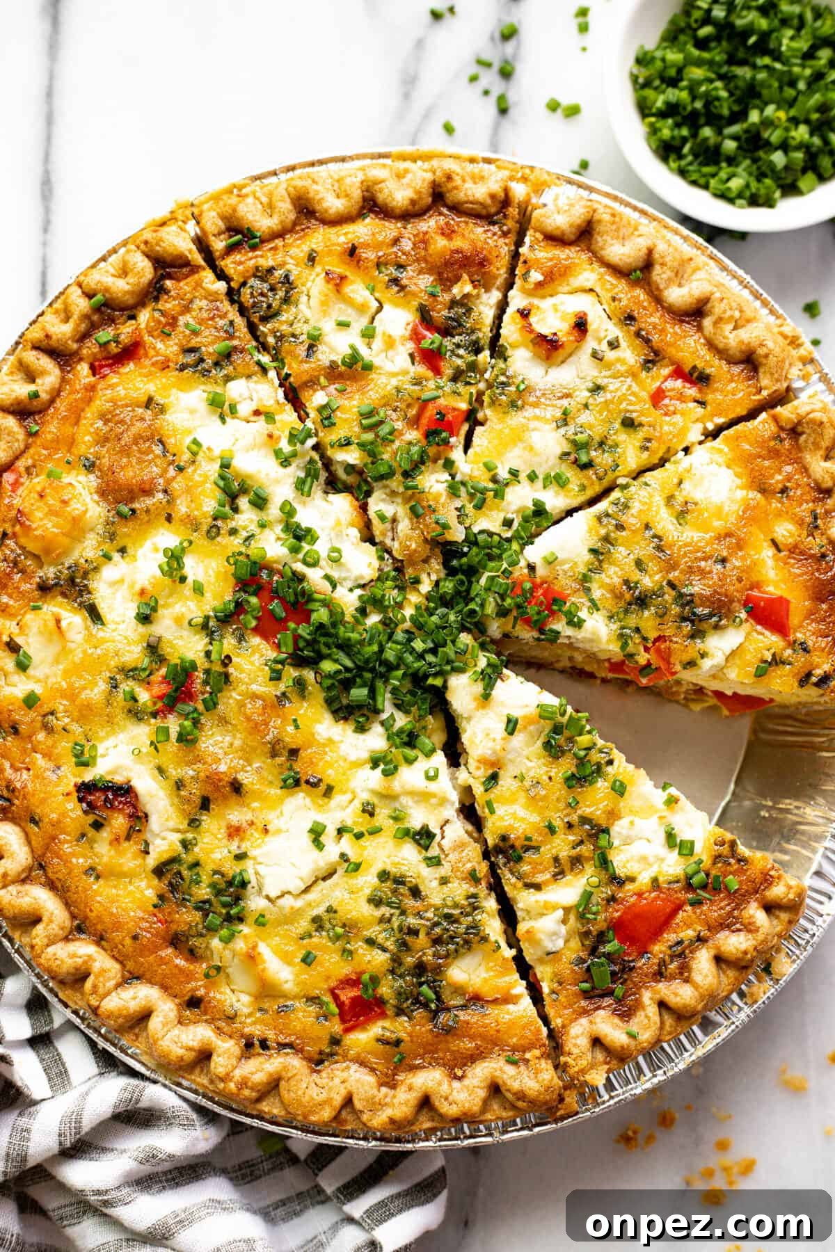 Quick Breakfast Quiche Recipe 13 Overhead shot of a sliced quiche with red peppers and potatoes garnished with sliced chives.