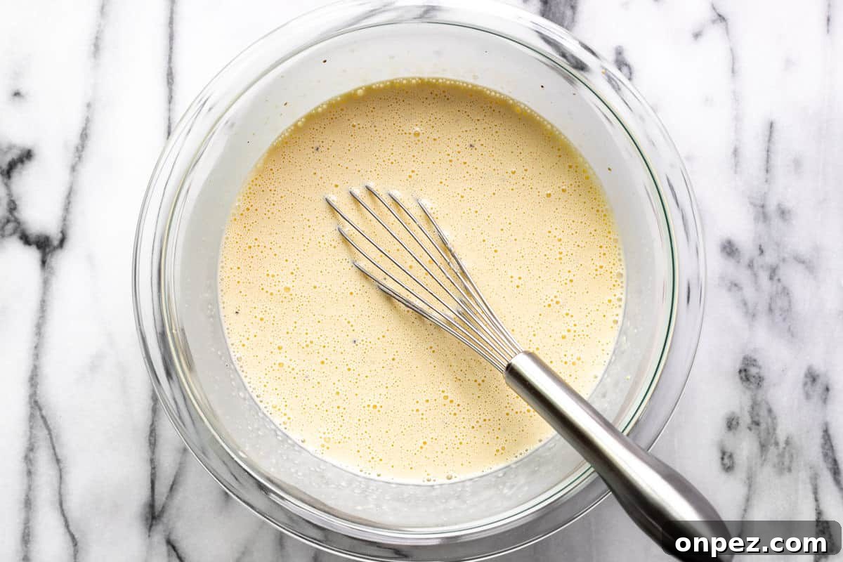 Quick Breakfast Quiche Recipe 6 The custard filling for the quiche in a large glass bowl with a whisk.