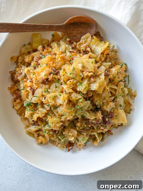 Homemade Hamburger Helper Recipe 4 A white bowl filled with a Deconstructed Cabbage Rolls mixture of cooked cabbage and ground meat, garnished with chopped herbs, sits on a light surface with a wooden spoon resting on the rim. A beige cloth is partially visible beside the bowl.
