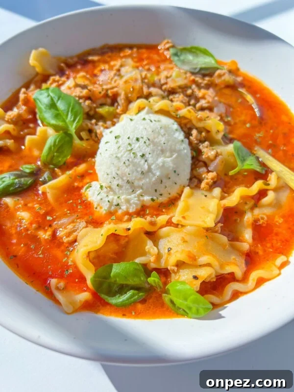 Homemade Hamburger Helper Recipe 7 A bowl of Lasagna Soup with ruffled pasta, tomato broth, ground meat, fresh basil leaves, and a scoop of ricotta cheese in the center.