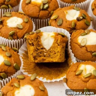 Gluten-free pumpkin cream cheese muffins on a countertop with a bite taken out of one of them.