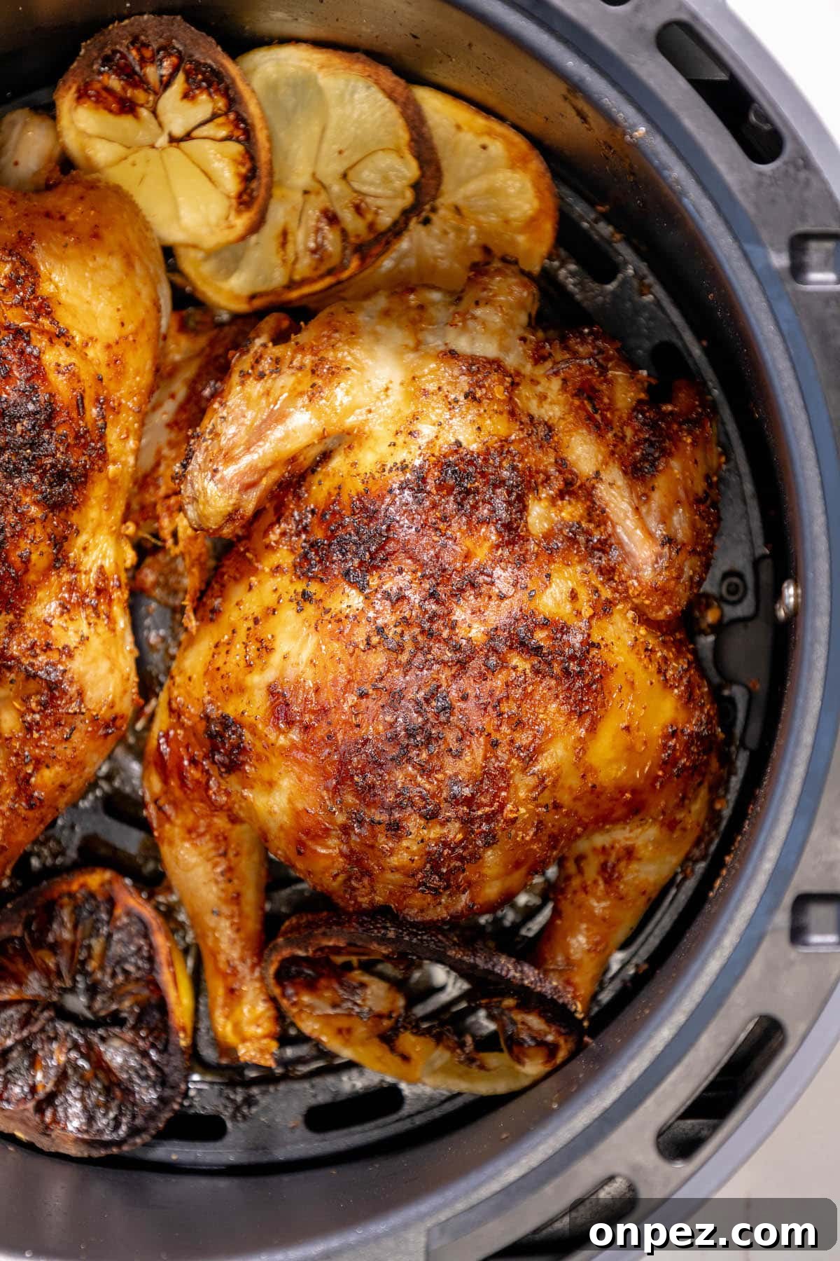 Crispy Air Fryer Cornish Hens Recipe with Herb Butter 3 air fried cornish game hens seasoned with herbs in an air fryer basket over slices of air fried lemons