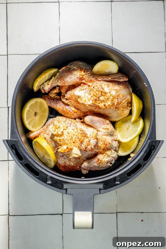 raw cornish game hens in an air fryer basket with seasonings and sliced lemons