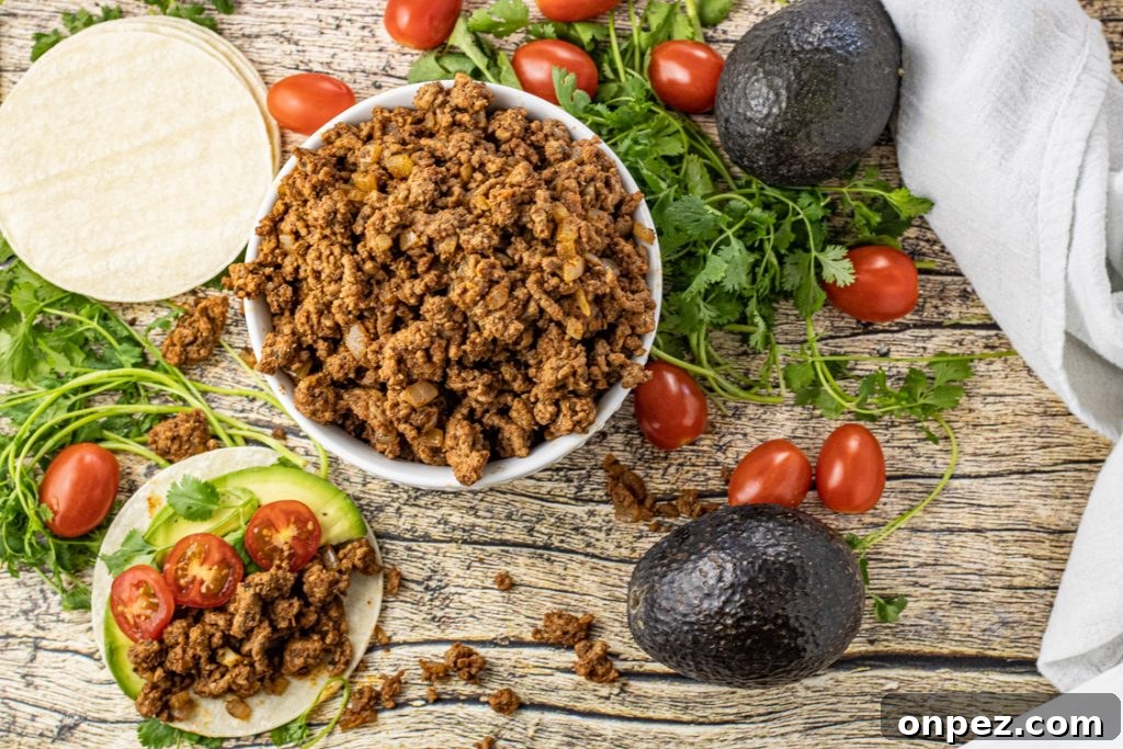 bowl of ground beef taco meat surrounded by avocados, cilantro and grape tomatoes