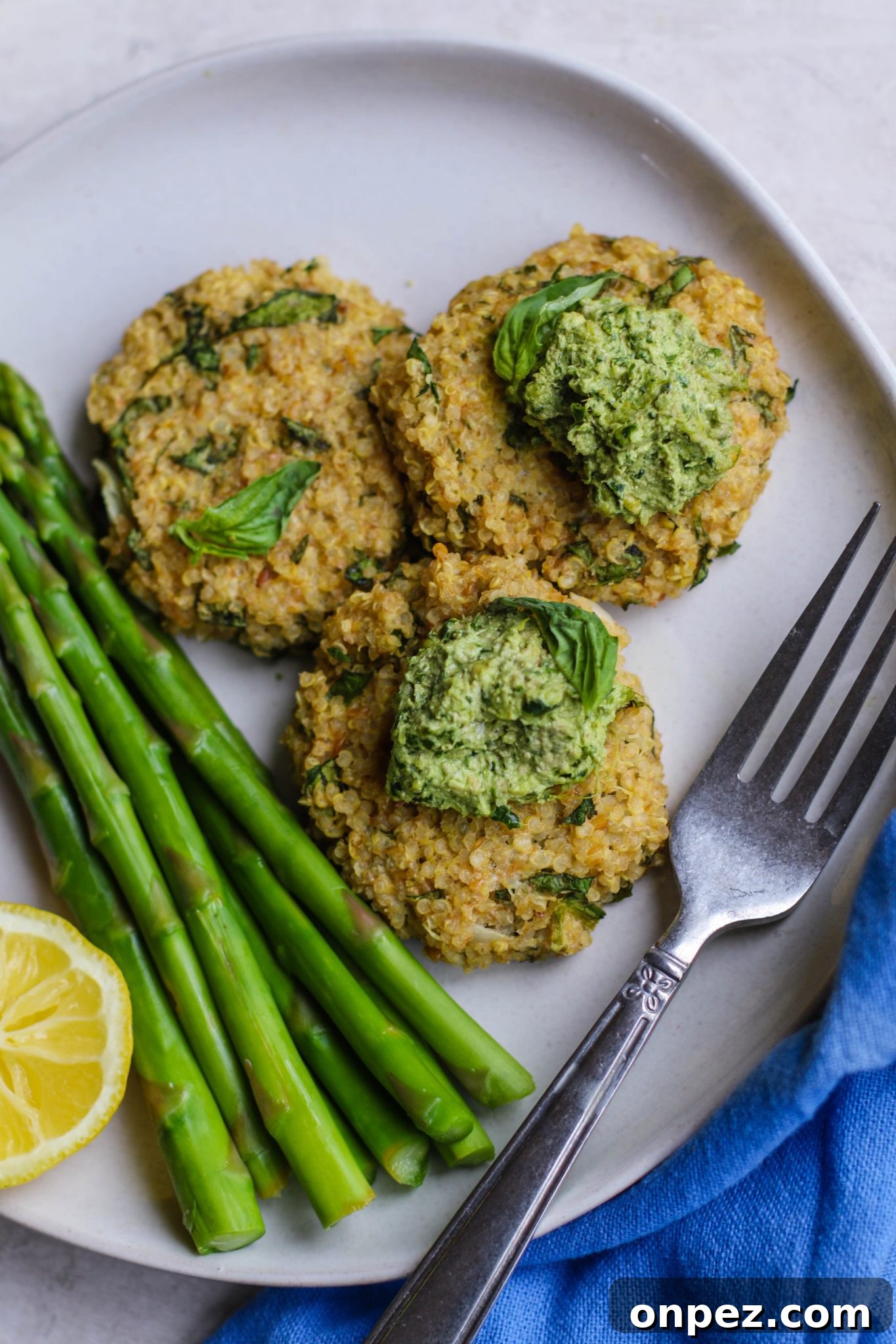 Quinoa Cakes with Basil Pesto served on plate with asparagus and a fork by Flora & Vino
