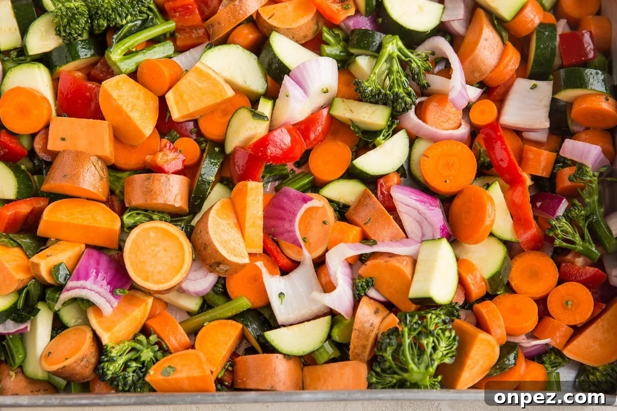 Raw vegetables seasoned with salt and oil in a large roasting pan, ready to go into the oven.