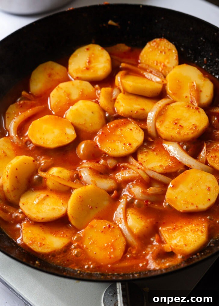 Potatoes simmering in spicy sauce in a skillet.