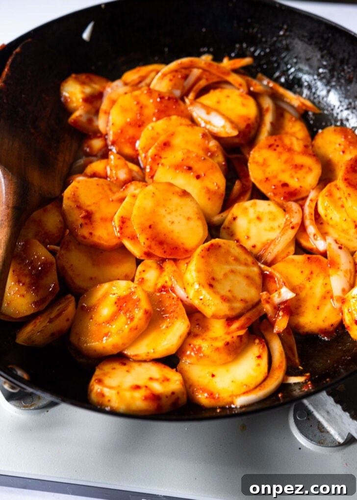 Spicy sauce added to the potato in a skillet.