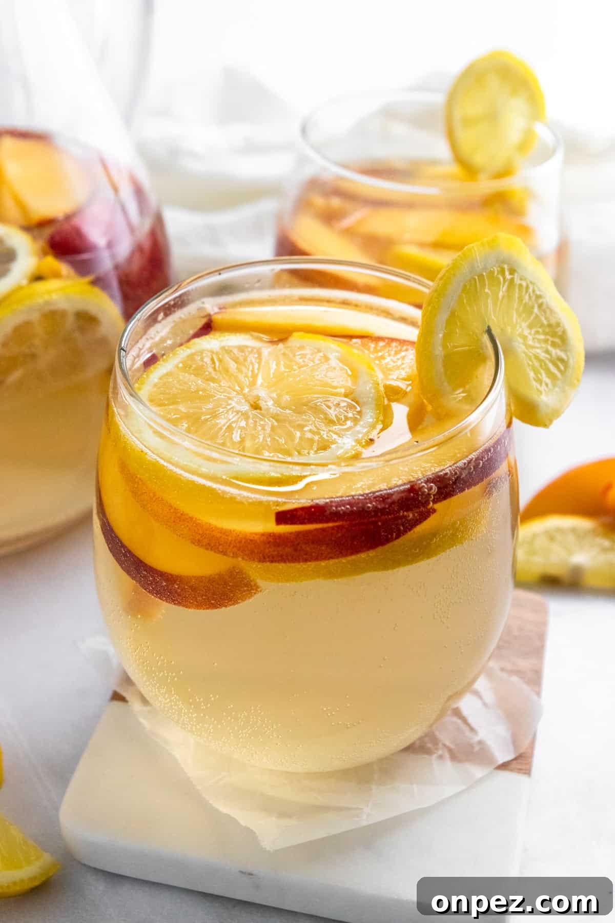 Ginger Peach White Wine Sangria Recipe 2 Ginger peach white sangria in glass with lemon slice on coaster.