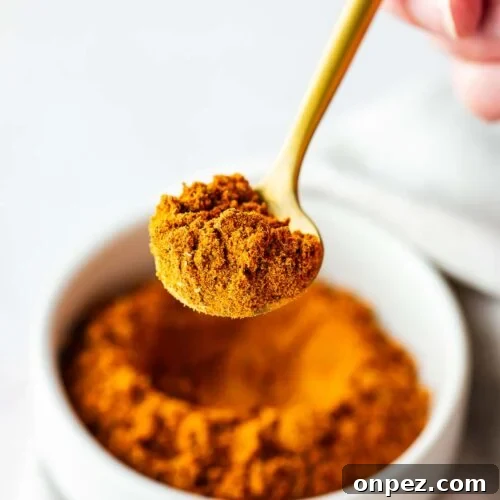 Close-up of homemade Old Bay Seasoning substitute on a gold teaspoon with a bowl of Old Bay in the background.