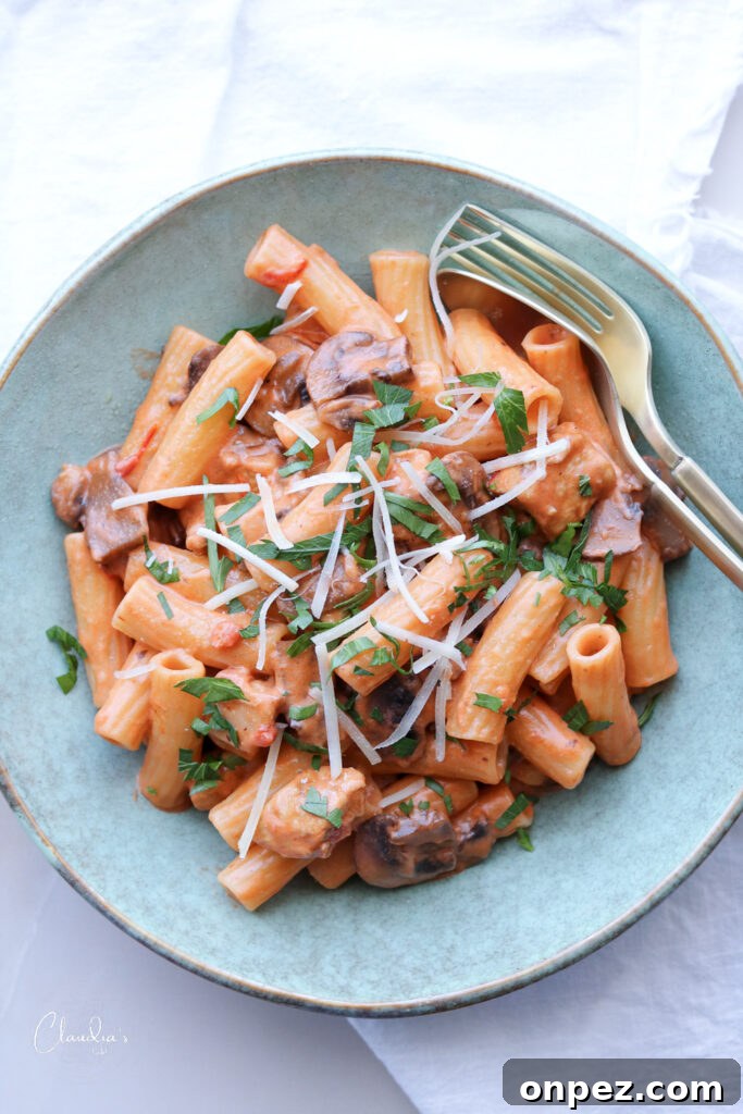 creamy tomato chicken and mushroom pasta in blue bowl with gold silverware